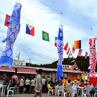 多くの人で賑わう商店街の屋外スペースにテーブルが設けられ、空には万国旗とともに大きくてカラフルなこいのぼりが吊るされている写真