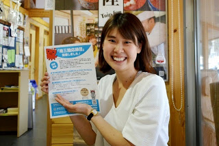 チラシを持つ星野奈々さんが笑顔で紹介している様子をアップで撮影した写真