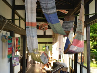 伝統的な日本家屋の廊下に色鮮やかな織物が吊るされており、自然光が差し込んでいる写真