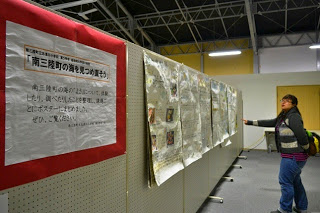 展示会場のような場所で人がパーティションに貼られたポスターや資料を見ている様子を写した写真