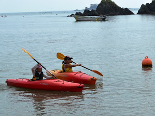 海の上で子どもが一人ずつ乗った赤いカヤックが2隻ならび、パドルを使って息を合わせて漕ぎながら水面を進んでいる様子を写した写真