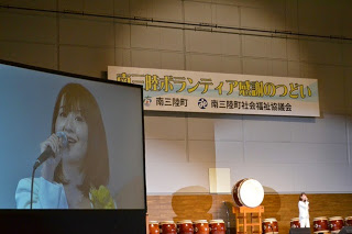 大きなモニターにマイクを持った女性が映っている写真