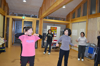 立った状態でリズムに合わせて腕を振るような動きをしながら楽しそうに運動している女性たちの写真