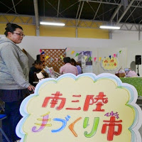 「南三陸手作り市（マルシェ）」とカラフルな色で書かれた手作りの看板が置かれた屋根付きの会場の写真