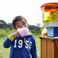 屋外に置かれた綿あめの機械の横で男の子がおいしそうに綿あめを食べている写真