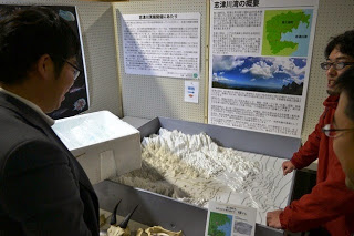 展示会で3人の人物が「立山連峰」に関する地形模型と説明パネルを見ている様子を写した写真