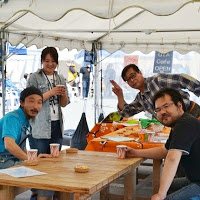 白いテントの下で4人の男女が木製のテーブルの周りに集まっている写真