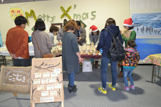 「Merry X'mas」の文字が飾られた壁の前のパン販売ブースの周りに買い物客が集まり、サンタクロースの帽子をかぶったスタッフが対応をしている様子の写真