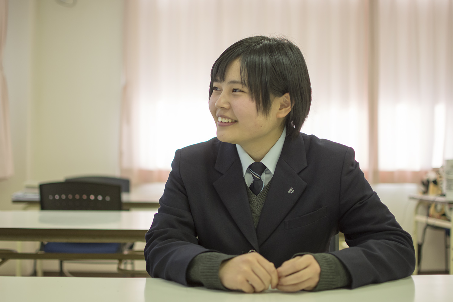 制服姿の三浦千裕さんが机の席につき、笑顔で横を向いている写真