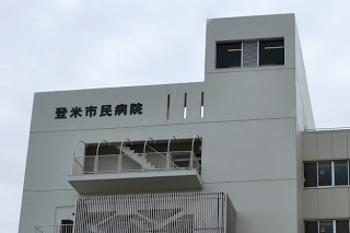「登米市民病院」と書かれた文字が見える白い外壁の病院建物の一部を写した写真