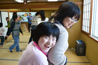 一人の女の子が笑顔で大人の女性にしがみついている様子を、近くから写した楽しげな場面の写真。