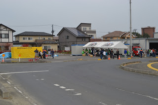 住宅街の広場に複数のテントが設置され、たくさんの人が集まり防災訓練や炊き出しを行っている様子を遠くから撮影した写真