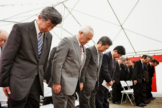 紅白幕が飾られたテントの中で、正装した関係者が整列し、一礼している安全祈願祭の様子の写真