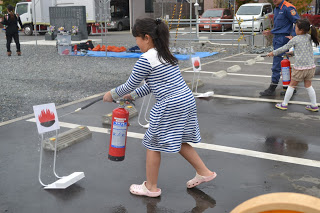 女の子が駐車場の一角で消火器を使って、紙に描かれた火の絵に向かって消火訓練をしている写真
