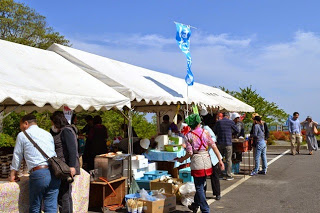 屋外の会場に並んだ白いテントの下に様々な商品がならび、たくさんの来場者が訪れている様子の写真