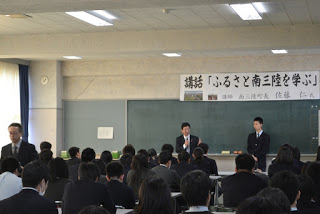 教室の前方に設置された「講話『ふるさと南三陸を学ぶ』」と書かれた横断幕が掲げられた黒板の前で佐藤町長と男子生徒が立ち、多くの生徒が座って町長の講話を聞いている様子の写真