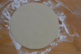 木の台の上に周囲には小麦粉がまかれ、丸く平らに伸ばされた生地が置かれている様子をアップで撮影した写真