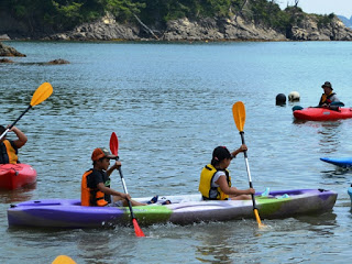 ライフジャケットを着た参加者たちが、2人1組でカヤックを漕ぎながら水面を進み、カヤックを楽しんでいる写真