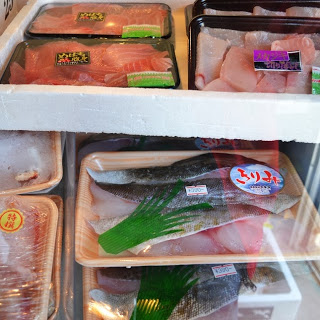 冷蔵棚の中に、発砲トレーに入った様々な種類の魚の切り身が包装され、ラベルが貼られて整然と並べられている様子が写っている写真