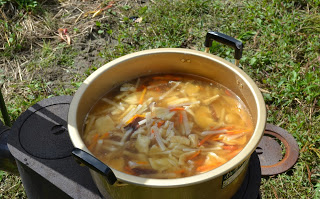 大鍋の中で大根、にんじん、きのこなどがたっぷり入った温かい味噌汁のような煮物が野外で火にかけられている写真