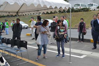 テントの下で料理を受け取った人たちが立って食べたり、並んで待ったりしている様子の写真