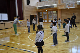 体育館で劇団四季の方が子どもに説明し、子どもたちが円形に並んで話を聞いている様子の写真