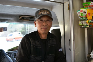 ロゴ入りの帽子と黒いジャケットを着用した佐々木店長の写真