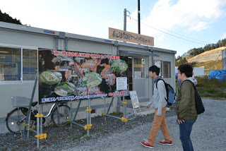 仮設建物の前に設置された大きな案内看板を、二人の若者が立ち止まって熱心に見ている写真