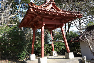 木々を背景に朱色の鐘楼が建っている写真