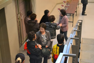 ホールの出口付近で和装や洋服を着た中高年の女性たちが話しながら出てきている様子の写真