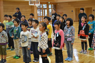 体育館で子どもたちが前を向いて並び、声を出して歌っている様子の写真