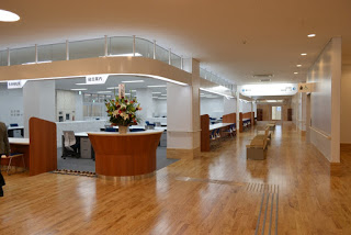 フローリングの床が広がり、中央左に花が飾られた受付があり、右側の広い通路にの中央に椅子が並んだ、明るく清潔感のある総合案内がある一角の写真