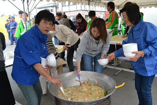 大きな鍋に入った具だくさんの汁物を女性たちが手分けして器に盛っている写真