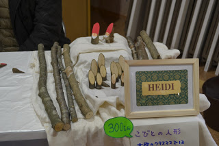 「HEIDI」と書かれた額縁に入った看板の下に「300円 こびとの人形」と書かれた案内が貼られ、後ろに小枝や、小枝を使った小さな人形などが並んでいるクリスマス飾りのコーナーの写真