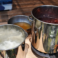 並べられた3つの鍋にそれぞれ白い羊毛、茶色の液体、赤い液体が入っている写真