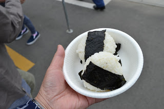 海苔で巻かれた三角おにぎりが2ケはいった白い紙皿を手に持っている写真