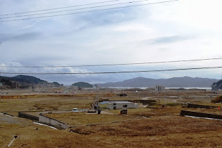 草原と丘が広がる風景の中に、建物が点在し、遠くに山々がそびえる広大な自然の写真