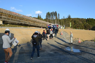 ヘルメットをかぶった多くの人たちが、復興工事中のエリアを整列して歩いて見学している写真