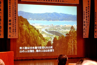 森と町と海を見渡す風景写真がスクリーンに大きく映され、「南三陸は分水嶺で区切られた町 山の人は海を、海の人は山を想う」と書かれた文字が表示されている写真
