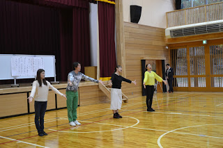 劇団四季の方々4人が横一列に並び腕を前に広げ伸ばし、大きな口を開けて立っている発声練習の見本を見せている写真