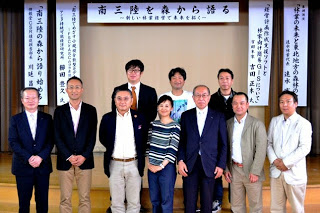 ステージ前で男性9人と女性1人が横二列に並び、「南三陸を森から語る」と書かれた垂れ幕の前で撮影された集合写真