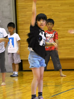 黒いシャツを着た女の子が右手を上にあげダンスの練習をしている様子を写した写真