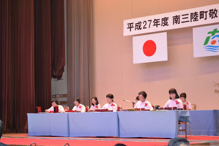 ステージ上でピンク色の衣装を着た女性たちが横一列に座って演奏をしている、楽器演奏の出し物の写真