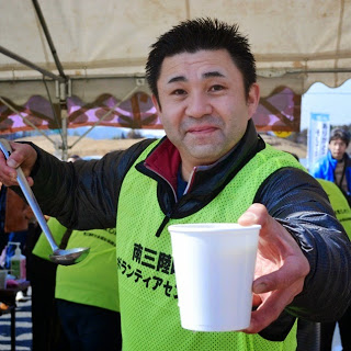 紙コップに汁ものを入れた男性が手渡ししている様子を写した写真