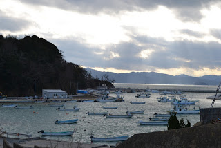 奥に山が見える海岸にたくさんの小舟が浮かんでいる写真