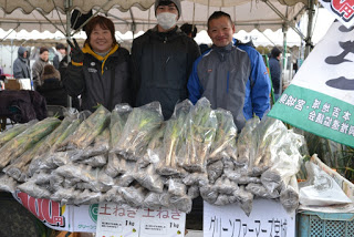 「土ねぎ 1キログラム」などが書かれたポップが貼られたテーブルには袋に入ったネギなどの野菜がずらりと並び、3人のスタッフが並んで立っている「グリーンファーマーズ宮城」の販売ブースの写真