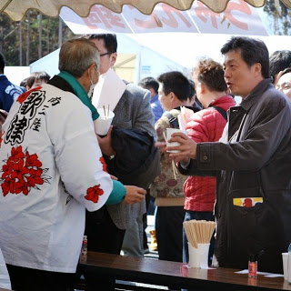 白い法被姿の男性が目の前の男性に汁物を手渡ししている写真