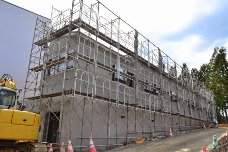 足場に囲まれ外壁工事が進められている、2階建ての集会所の建物の全体の外観写真