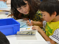 男の子が机に向かって塗り絵をしており、横から女性が覗き込んでいる写真