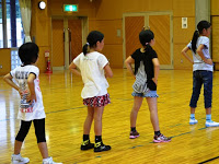 4人の女の子が横一列に並んで立ち、それぞれが両手を腰において横を向いたポーズを取っている様子が写された写真